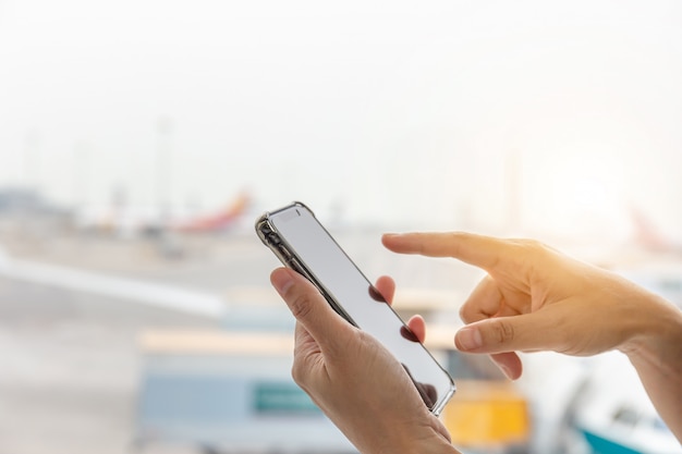 Schließen Sie oben von der Hand der jungen Frau unter Verwendung des mobilen Smartphone im undeutlichen Hintergrund des Terminals.