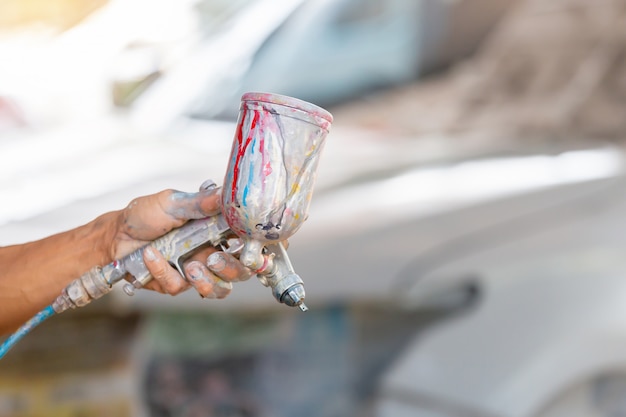 Schließen Sie oben von der Hand des Autoreparaturmannmalers, die eine Sprühpistole über unscharfem Hintergrund hält