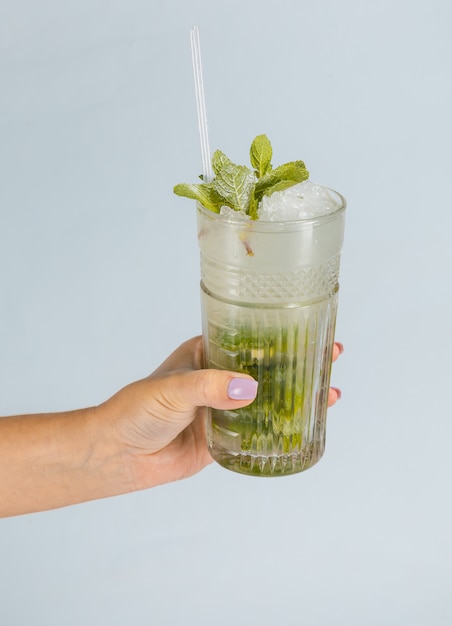 Schließen Sie oben von der Hand einer Frau, die ein Glas des tropischen Mojito-Cocktails auf orange Oberfläche mit Kopienraum hält. Sommerferienkonzept.