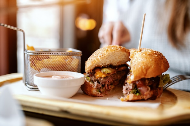 Schließen Sie oben von der kaukasischen Frau, die köstlichen Burger während des Sitzens im Restaurant isst.