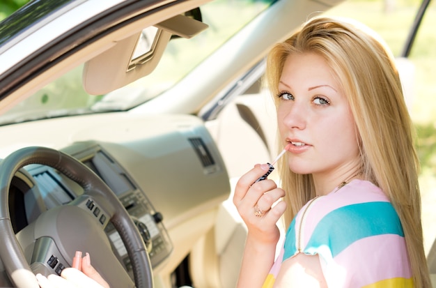 Schließen Sie oben von einem attraktiven blonden Mädchen, das Lipgloss anwendet, das die Kamera betrachtet.