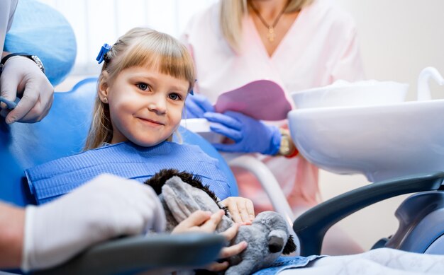 Schließen Sie oben von einem kleinen niedlichen Mädchen, das mit glücklichem Lächeln im stomatologischen Stuhl sitzt