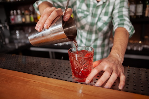 Schließen Sie oben von einem männlichen Bartebder, der ein Getränk zum Glas gießt. Professioneller Barkeeper, der Cocktail für einen Kunden vorbereitet