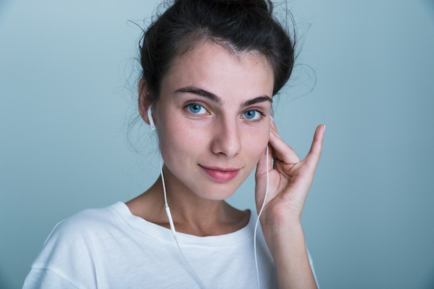 Schließen Sie oben von einem schönen jungen lässigen Mädchen, das lokal über blauem Hintergrund steht und Musik mit Kopfhörern hört