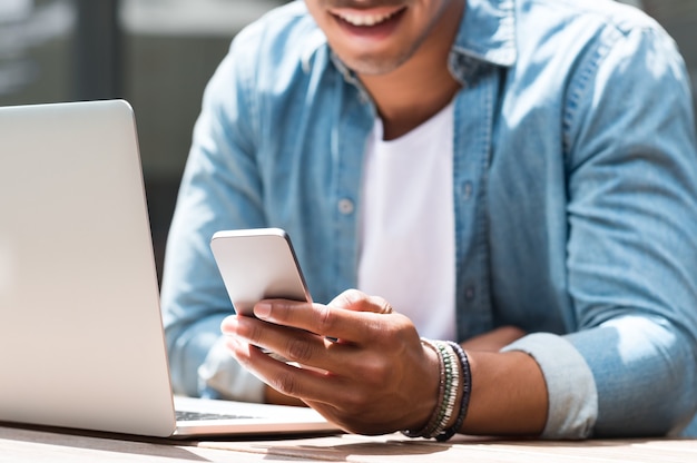 Schließen Sie oben von einem Studentenmann, der Smartphone und Laptop im Café verwendet