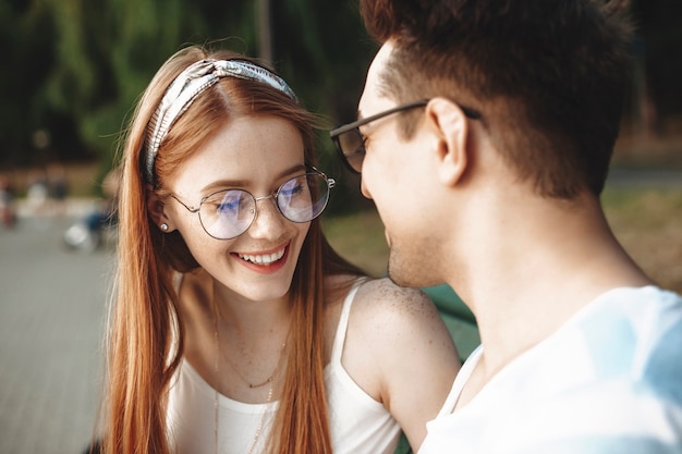 Schließen Sie oben von einer attraktiven jungen rothaarigen Frau mit Sommersprossen, die mit geschlossenen Augen lachen, während Sie mit ihrem Freund draußen im Park datieren.