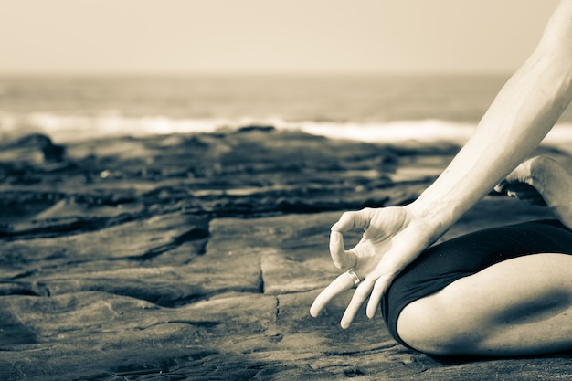 Schließen Sie oben von einer Frau, die Yoga auf den Felsen durch das Meer in Goa, Indien praktiziert. Yogi am Strand. Meditation, Achtsamkeit, Naturverbindungskonzept