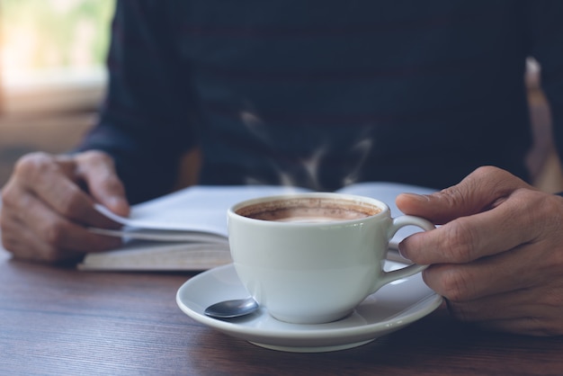 Schließen Sie oben von Mann, der ein Buch und eine Tasse Kaffee auf Tisch liest