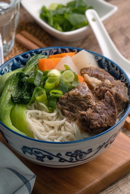 Schließen Sie oben von taiwanesischem berühmtem Essen mit geschnittenem geschmortem Rindfleischschenkel und Gemüse in einer Schüssel auf Holztisch