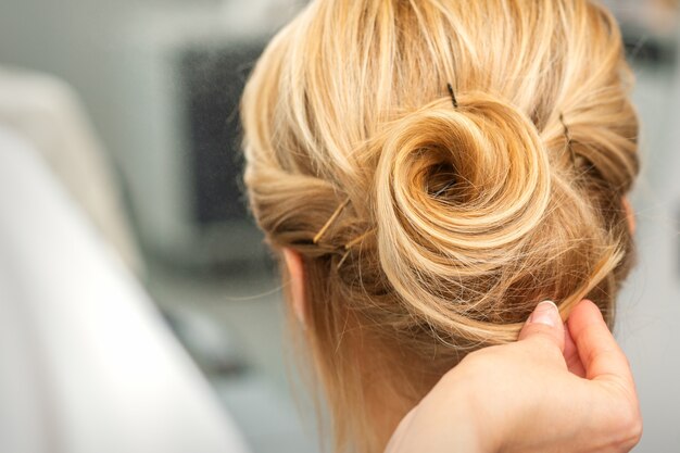 Schließen Sie oben von weiblichem Friseur, der blondes Haar einer jungen Frau in einem Schönheitssalon stylt