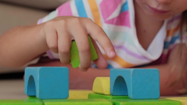 Foto schloss die hände des konzentrierten kindes mädchen zu hause spielen mit farbigen holzblöcken auf flor.