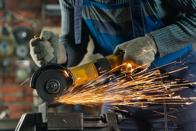 Schlosser in Spezialkleidung und Schutzbrille arbeitet in der Metallbearbeitung mit Winkelschleifer