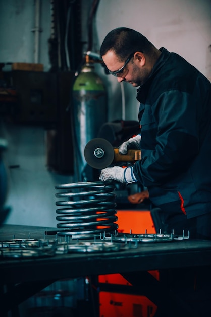 Schlosser in Spezialkleidung und Schutzbrille arbeitet in der Produktion Metallbearbeitung mit Winkelschleifer Funken in der Metallbearbeitung