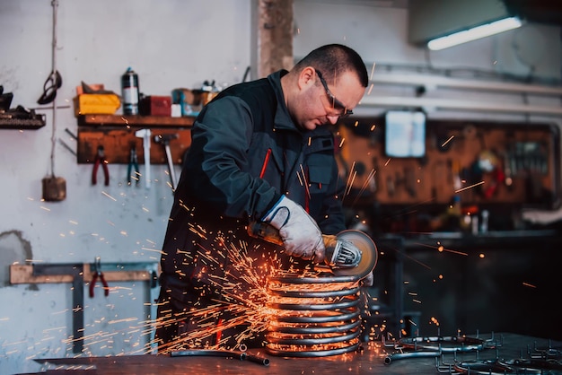 Schlosser in Spezialkleidung und Schutzbrille arbeitet in der Produktion Metallbearbeitung mit Winkelschleifer Funken in der Metallbearbeitung