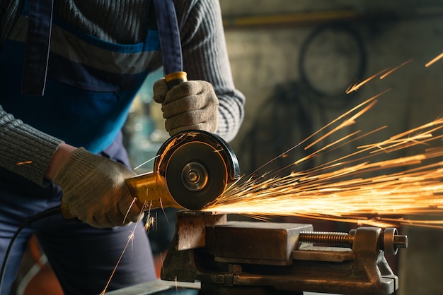 Schlosser in Spezialkleidung und Schutzbrille arbeitet in der Produktion. Metallbearbeitung mit Winkelschleifer