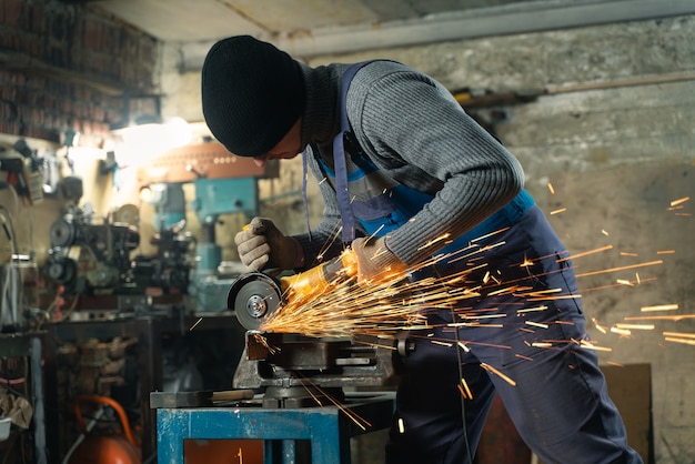 Schlosser in spezialkleidung und schutzbrillen arbeitet in der produktion metallbearbeitung mit winkelschleifer