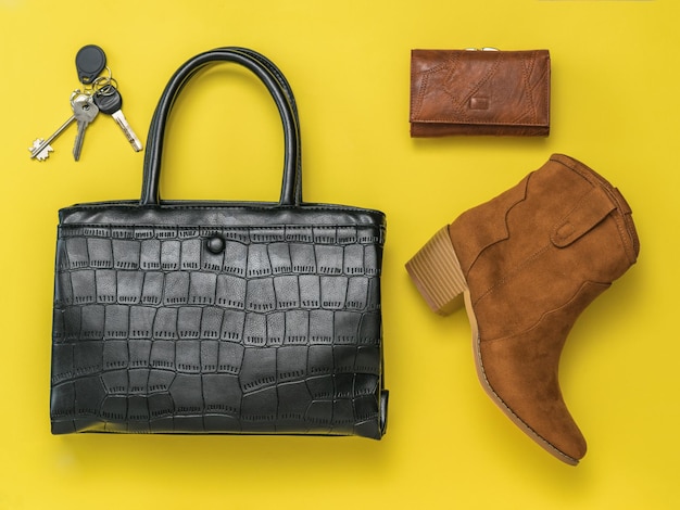 Schlüssel, Tasche, Geldbörse und Stiefel auf gelbem Grund. Modische Damenaccessoires aus Leder. Flach liegen.