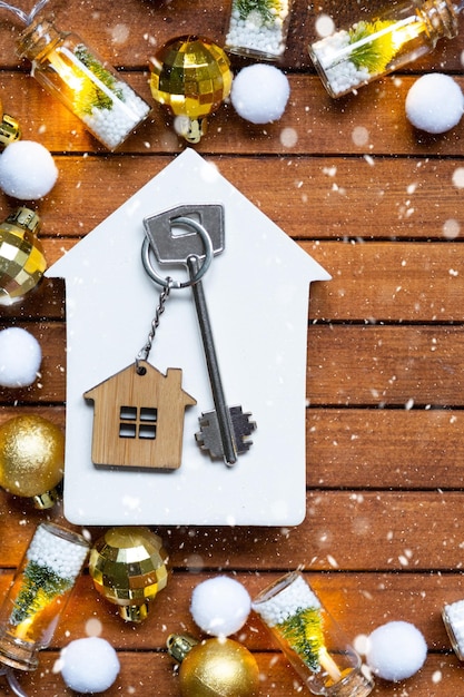 Schlüssel zum Haus mit einem Schlüsselanhänger, kleines Haus auf hölzernem Hintergrund mit Weihnachtsdekorationslayout