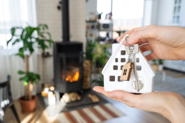 Schlüssel zum Haus mit Schlüsselanhänger vor dem Hintergrund des Kaminofens mit Feuer und Brennholz