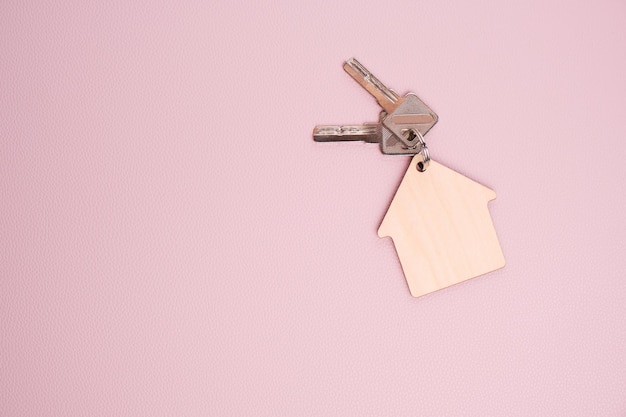 Schlüsselanhänger in Form Haus mit Schlüsseln rosa HintergrundKonzept Kauf Haus Wohnung oder Miete