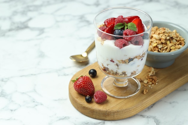 Schmackhafter Joghurt mit frischen Beeren und Muesli in einer Glas-Dessertschüssel auf einem weißen Marmor-Tisch in Nahaufnahme Platz für Text