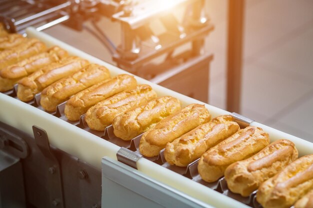 Schmaler Förderer mit Eclairs Gebäck auf Förderband Komplexer Mechanismus für die Lebensmittelproduktion Die Industrie schreitet voran