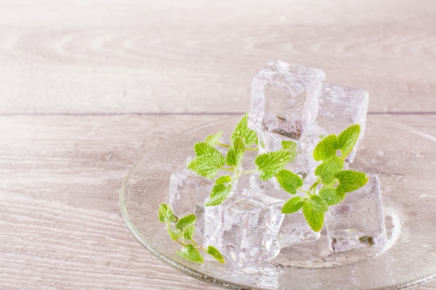 Schmelzende Eiswürfel und tadellose Blätter auf einer Untertasse auf einem Holztisch