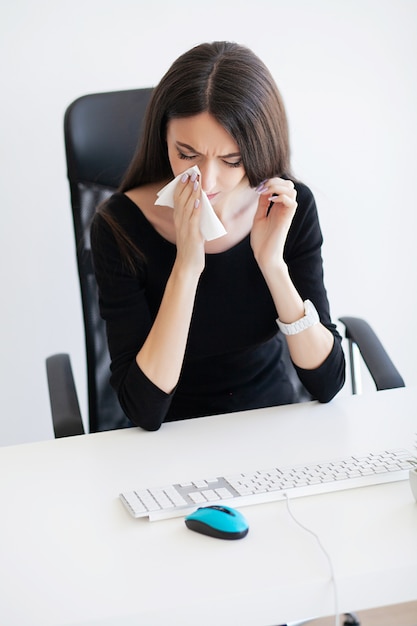 Schmerzen. Kranke Geschäftsfrau, die bei der Arbeit hinter dem Schreibtisch in ihrem Büro leidet und Allergieproblem hat.
