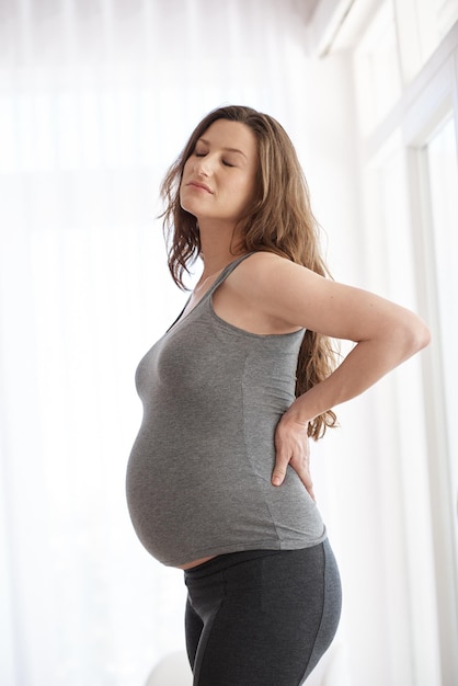 Schmerzen Schnappschuss einer jungen schwangeren Frau, die ihre Hände vor Unbehagen auf ihren unteren Rücken legt
