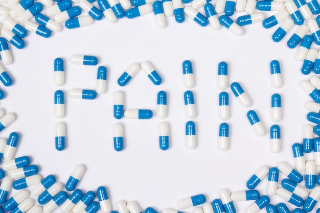 Schmerzworttext aus blauen Tabletten, Pillen und Kapseln auf weißem Hintergrund