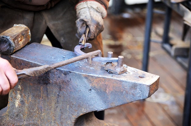 Schmied bearbeitet Metall mit Hammer auf dem Amboss in der Schmiede