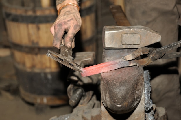 Schmied, der in der Schmiede arbeitet, verarbeitet das Metall. Das Foto zum Thema Schmiedekunst