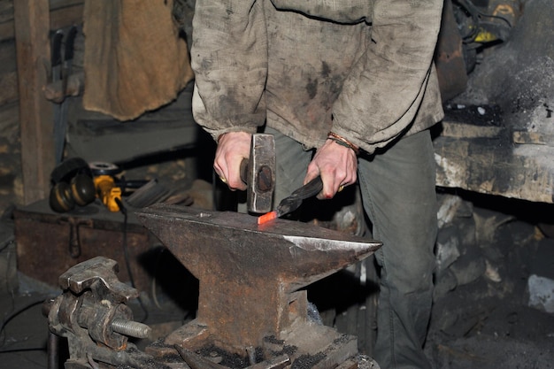 Schmied, der Metall mit Hammer auf dem Amboss in der Schmiede bearbeitet