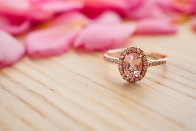 Schmuck rosa Diamantring auf Holztisch mit schönem Rosenblütenhintergrund aus nächster Nähe