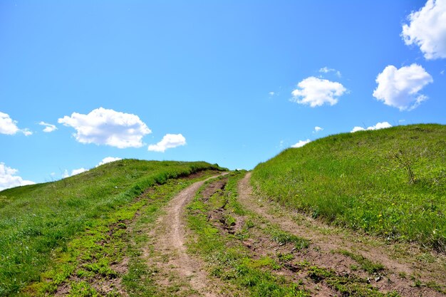 Schmutzige Landstraße, die den Hügel hinaufgeht, mit blauem Himmel und Wolken im Hintergrund