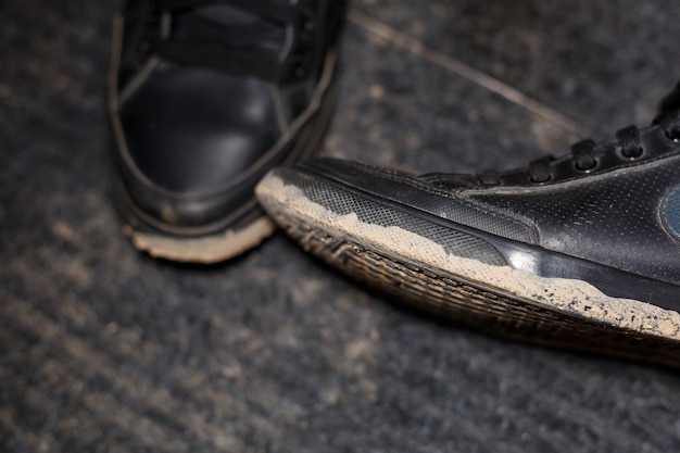 Schmutzige Schuhe stehen auf einem schwarzen Teppich mit verstreutem Sumpf