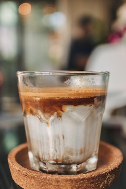 Schmutziger Kaffee in transparentem Glas, serviert auf schwarzem Tablett im Café