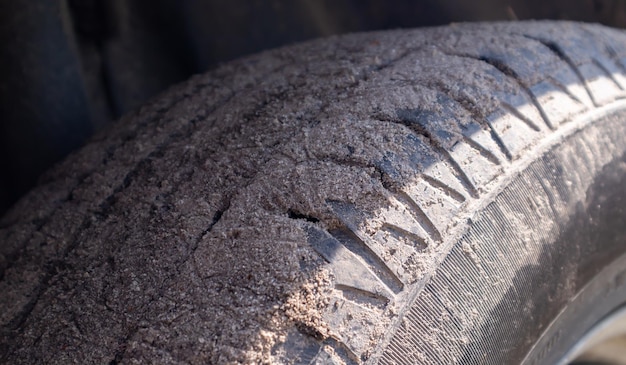 Schmutziges Autorad auf einer Bodenstraße zur Landschaft. Nahaufnahmedetail eines Reifens. Transport-, Fahr- und Autokonzept. Das Auto blieb im Sand stecken.