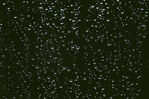 Schmutziges Fensterglas mit Regentropfen. Atmosphärischer grüner Hintergrund mit Regentropfen. Tröpfchen und Flecken schließen sich. Detaillierte transparente Textur im Makro mit Kopierraum. Regnerisches Wetter.