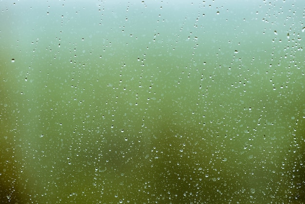 Schmutziges Glas mit Tropfenregen. Regentropfen auf grünem klarem bokeh. Grün vor dem Fenster. Tröpfchen und Flecken hautnah. Ausführliche transparente Beschaffenheit im Makro.