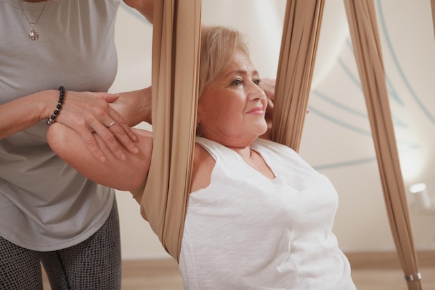 Schnappschuss einer älteren Frau, die einen Aerial Yoga-Kurs mit einem professionellen Yogalehrer genießt