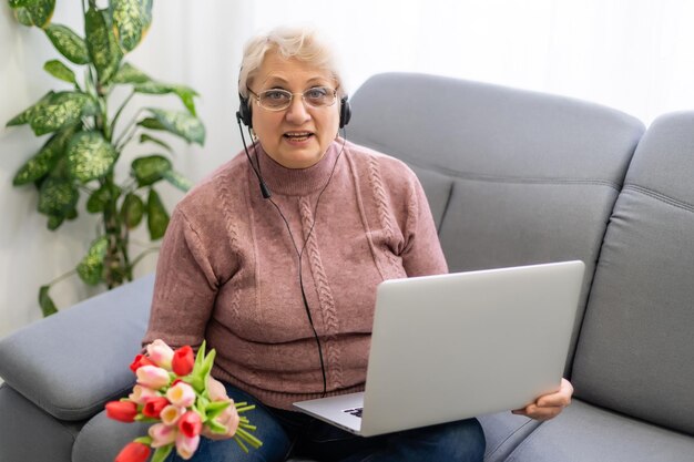 Schnappschuss einer schönen älteren Frau, die einen Laptop benutzt, während sie mit Blumen sitzt.