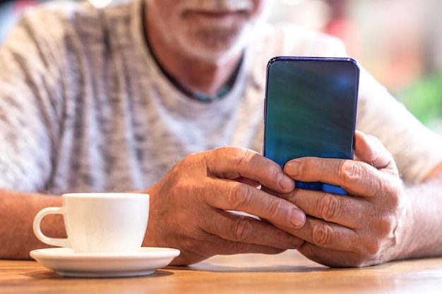 Schnappschuss eines gutaussehenden älteren Mannes, der die Nachricht auf dem Handy überprüft, während er in der Cafeteria Kaffee trinkt Mann, der ein Smartphone verwendet, während er Espressokaffee trinkt