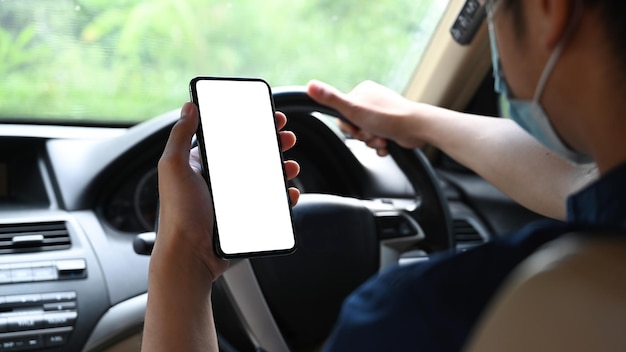 Schnappschuss eines jungen Mannes mit Schutzmaske und Smartphone beim Autofahren