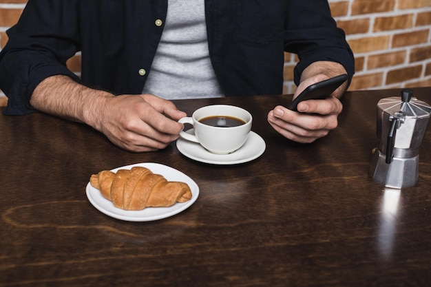 Schnappschuss eines jungen Mannes mit Smartphone, während er morgens zu Hause Kaffee trinkt