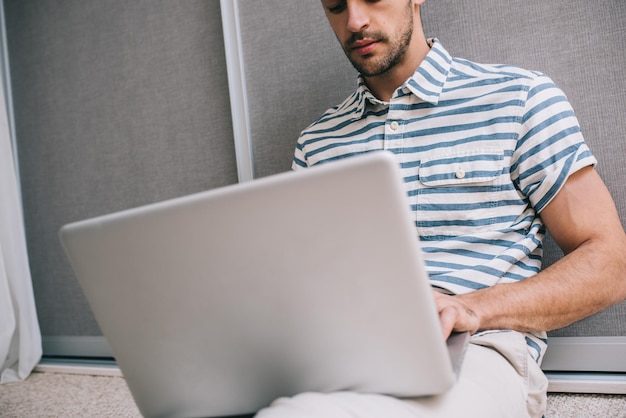 Schnappschuss fröhlicher junger europäischer Mann in stylischem Hemd, der zu Hause auf dem Boden sitzt, mit Laptop-PC auf dem Schoß, Videoanruf für Unternehmensgründung Menschen und Lifestyle-Konzept