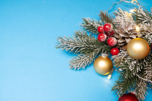 Schnee bedeckter Weihnachtsbaumzweig mit roten und goldenen Kugeln auf blauem Hintergrund