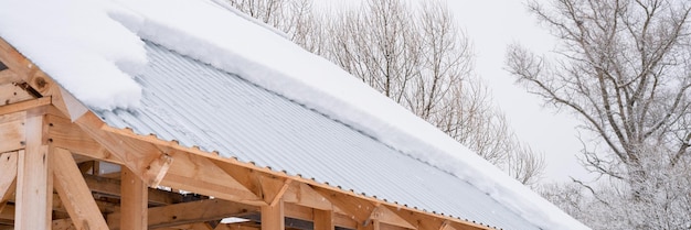 Schnee, der vom Dachgebäude herunterrutscht, Bauhaus mit Metalldach, bedeckt mit frischem, eisigem, gefrorenem Schnee und Schneeflocken am frostigen Wintertag im Vorort des Landdorfs, schneebedecktes Wintersaison-Banner