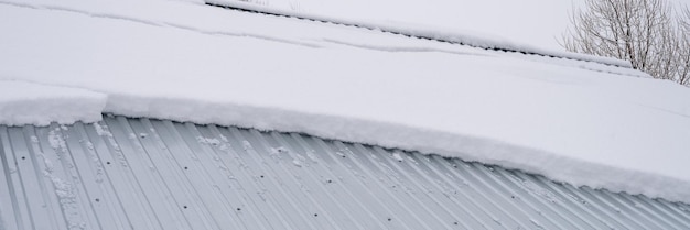 Schnee, der vom Dachgebäude herunterrutscht, Bauhaus mit Metalldach, bedeckt mit frischem, eisigem, gefrorenem Schnee und Schneeflocken am frostigen Wintertag im Vorort des Landdorfs, schneebedecktes Wintersaison-Banner