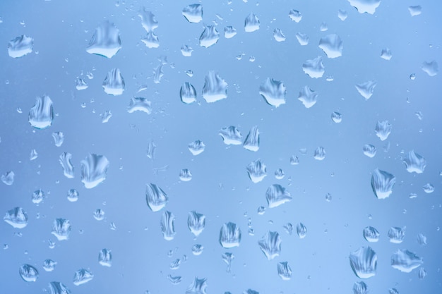 Schnee schmilzt am Fenster mit blauem Glas. Wassertropfen.